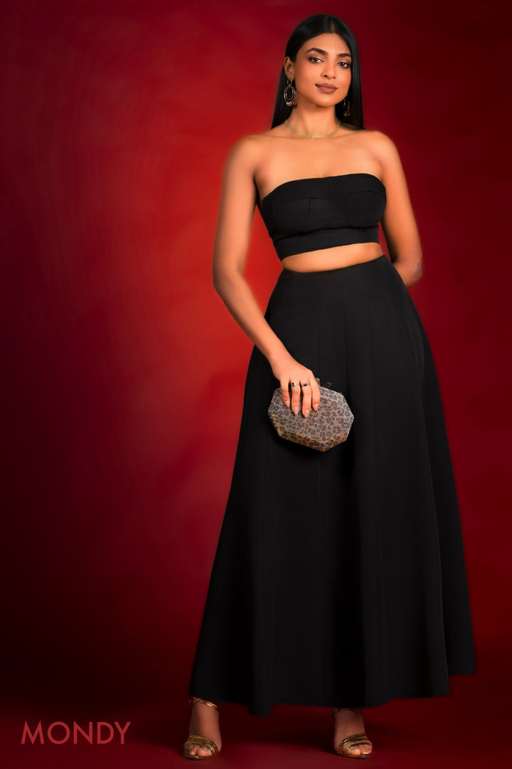 Woman in a black strapless top and long skirt holding a clutch against a red background
